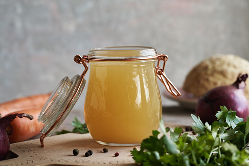 Chicken bone broth or soup in a glass jar with herbs and vegetables