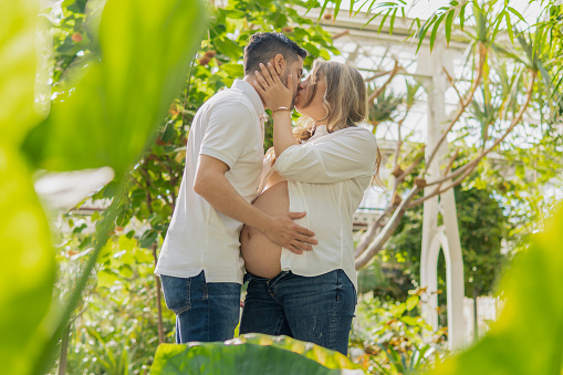 Pregnant latin lady kissing boyfriend on exotic garden