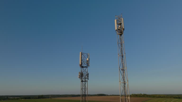 Two radio towers in the middle of farmland during sunrise, aerial orbital dolly in tilting upward