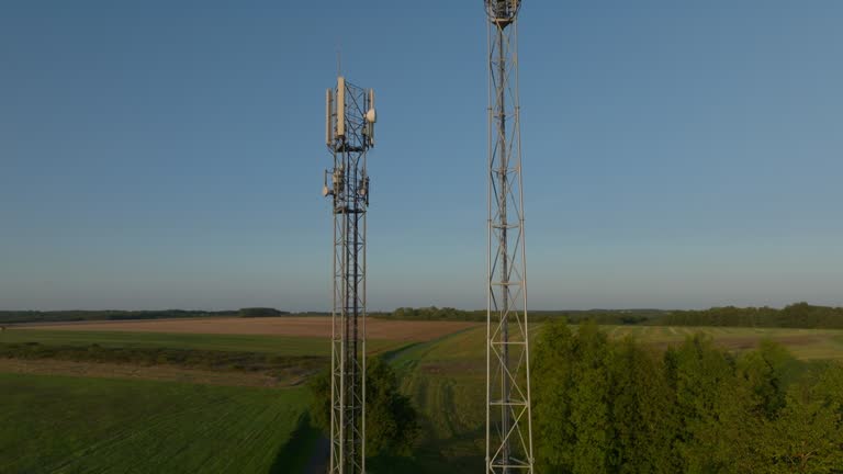 Two radio towers in the middle of farmland during sunrise, aerial orbital dolly in tilting upward