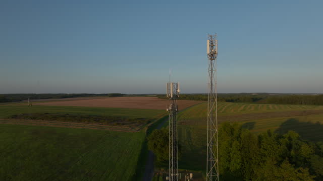 Two radio towers in the middle of farmland during sunrise, aerial orbital dolly in tilting
