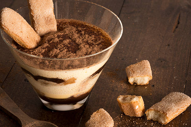 Tiramisu cup Tiramisu of mascarpone cream, biscuit and cocoa in a glass cup over wood table tiramisu glass stock pictures, royalty-free photos & images