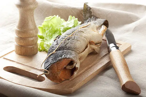 Trunk of salmon, lettuce, knife and salt-shaker on the wooden board