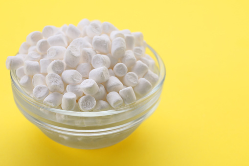 Glass bowl with delicious marshmallows on yellow background, closeup
