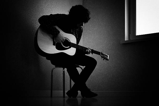 Black and white photo of man playing guitar Man sitting on stool in dark room playing guitar acoustic guitar photos stock pictures, royalty-free photos & images