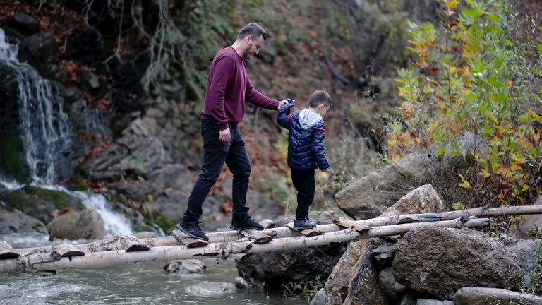 man walking with his son across a wooden footbridge over a stream