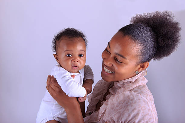 Ethnic mother and daughter playful kissing with nose dressed in pink and yellow background