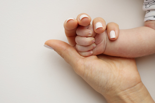 Parents' hands hold the fingers of a newborn baby. The hand of a mother and father close-up holds the fist of a newborn baby. Family health and medical care. Professional photo on white background.