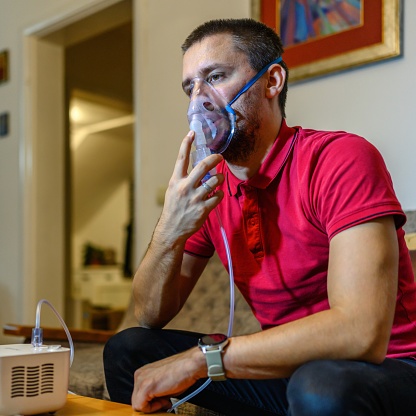 A sick man inhaling through an inhaler mask sitting on the sofa.