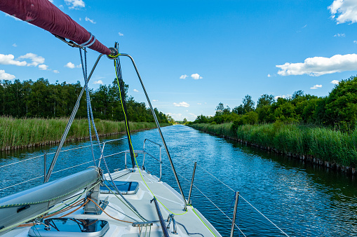A yacht sailing through a canal with the mast folded in the Masurian Lake District. Great Masurian Lakes.