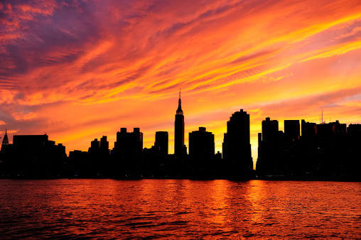 New York City Manhattan midtown silhouette panorama at sunset with skyscrapers and colorful sky over east river