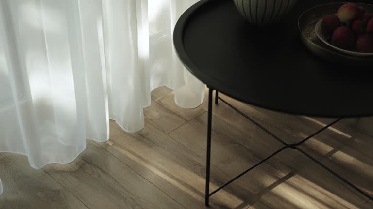 Close-up of black metal round table and shadows on the floor from the window and sun rays through the tulle on the chairs, slow motion.