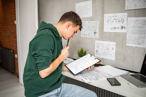 A young teenage student is studying at home, sitting at a desk, his books are on the table