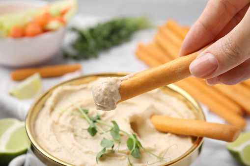 Woman dipping grissini stick into hummus at table, closeup
