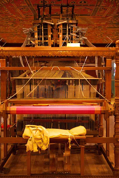 The weaver's chair on the rear of a large wooden handloom in the process of making a pink Indian sari