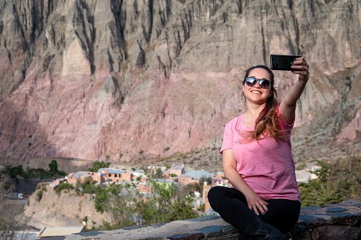 Woman taking a selfie and in the background the beautiful and colorful mountains of northern Argentina. Tourist taking a photo of the beautiful town of Iruya, Salta, Argentina. Tourist touring northern Argentina.