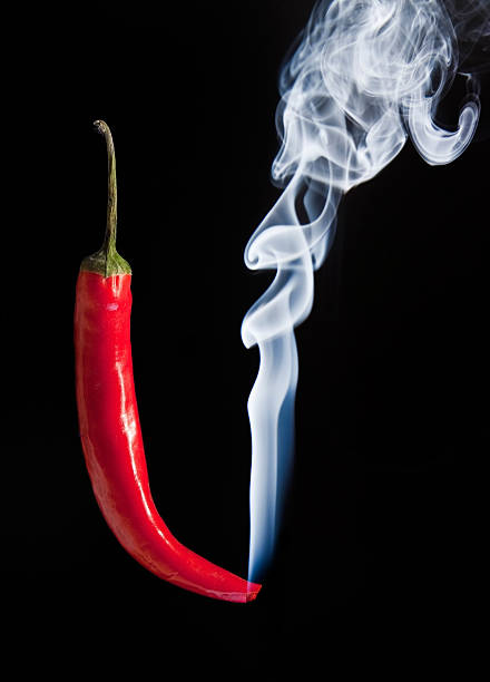 Red hot chilli pepper with smoke coming out of tip which is burning and glowing