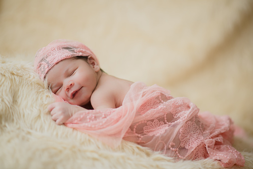 Adorable newborn girl smiles as she sleeps covered in delicate pink blanket