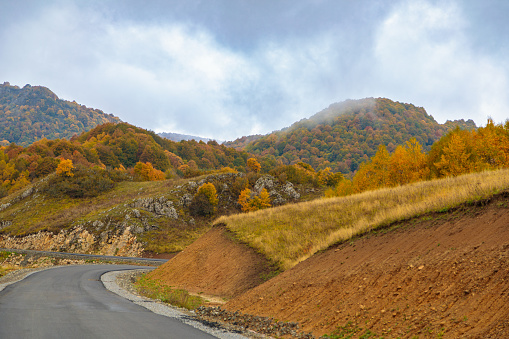 Winding road to the mountains. Sunny autumn in the mountains covered with bright colorful trees