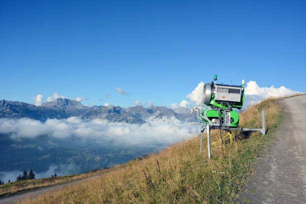 On a mountain slope above the clouds on a bright day, there is a cannon for making artificial snow