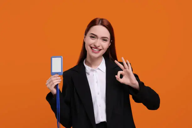 Photo of Happy woman with VIP pass badge showing OK gesture on orange background