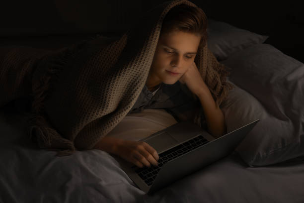 istock Teenage boy using laptop under blanket on bed at night. Internet addiction 1786384220