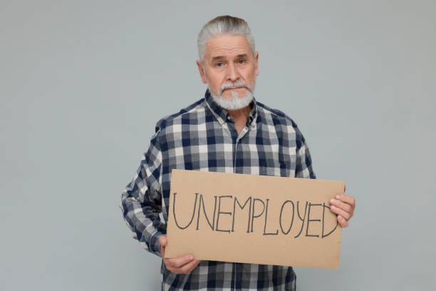istock Senior man holding cardboard sign with word Unemployed on light grey background 1786384547