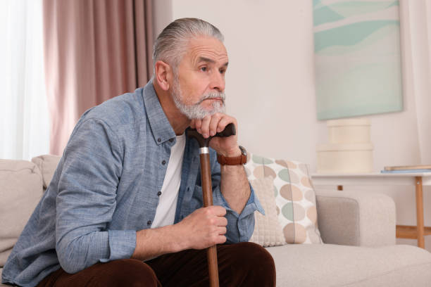 istock Senior man with walking cane sitting on sofa at home. Space for text 1786385321