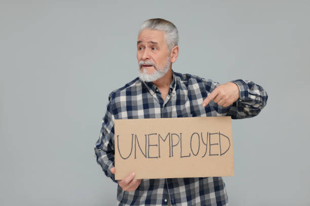 istock Senior man pointing at cardboard sign with word Unemployed on light grey background 1786387999