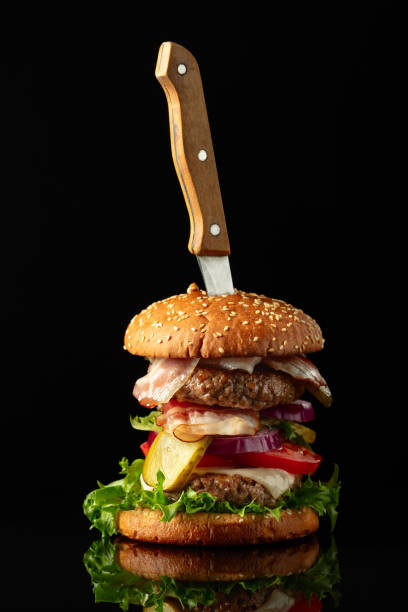 Fresh tasty burger with knife on a black reflective background.