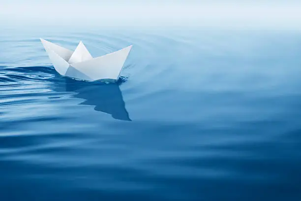 paper boat sailing on blue water surface.