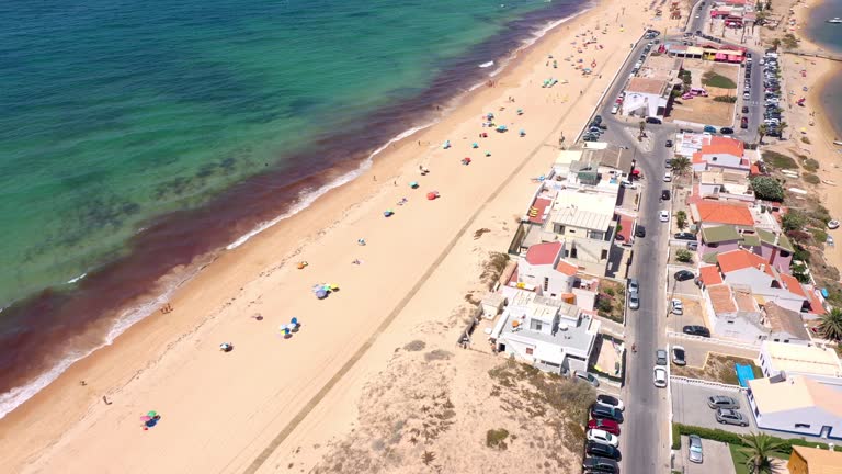 Aerial view of ocean coast and beach. Boats on the water and tourists relaxing on beach as seen from a drone. Praia de Faro Algarve Portugal. road in the middle of the island