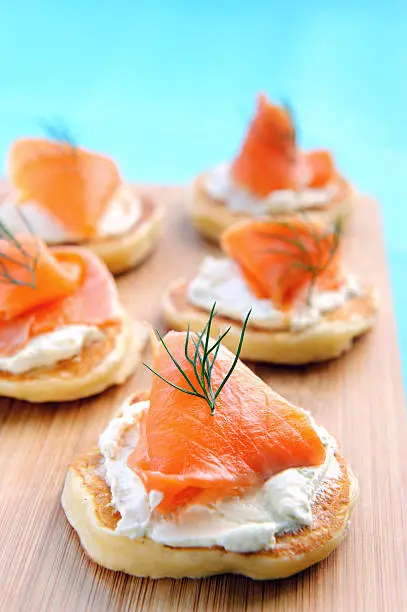 Mini pancakes topped with cream cheese and smoked salmon on a wooden platter