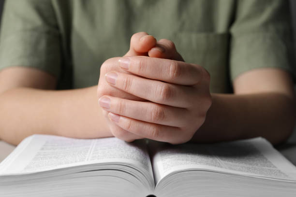 istock Woman holding hands clasped while praying over Bible at table, closeup 1786415573