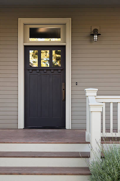 Front Door of an Upscale Home Front view of a black front door with white trim on a gray house, with view of front steps and porch light. Vertical shot.  doorstep stock pictures, royalty-free photos & images