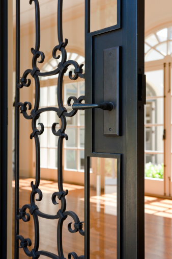 View of a glass and wrought Iron door and handle from the right with view of room and other architecture in background. Vertical shot.