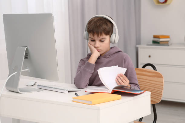 istock Boy reading book near computer at desk in room. Home workplace 1786439252