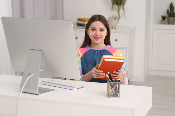 istock Cute girl with books using computer at desk in room. Home workplace 1786439255