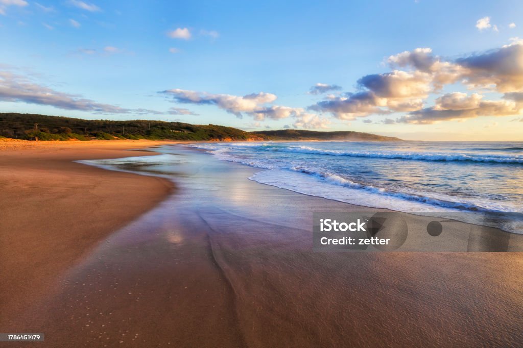 CHB FLat beach sand wave to north Flat sunlit Middle camp beach at Catherine hill bay town on Pacific coast of Australia at sunrise. Australia Stock Photo