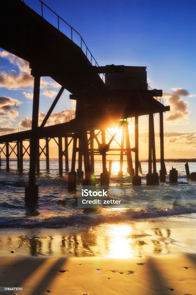 CHB Jetty Sun beach under vert Under historic massive timber jetty off MIddle camp beach in Catherine hill bay town on Pacific coast of Australia at sunrise. Australia Stock Photo