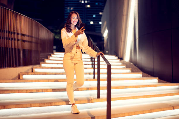 istock Young woman using mobile phone during walk in the night city, going down the illuminated stairs, copy space, full length 1786488052