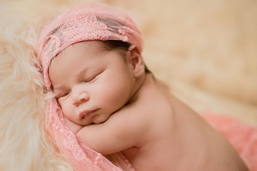 Adorable newborn girl sleeps calmly upside down leaning from her arms. Pink accessory on her head