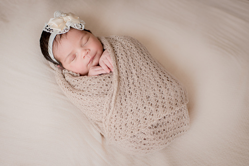 Newborn Photo: Baby girl sleeps covered with a delicate Beige blanket on a soft Beige background