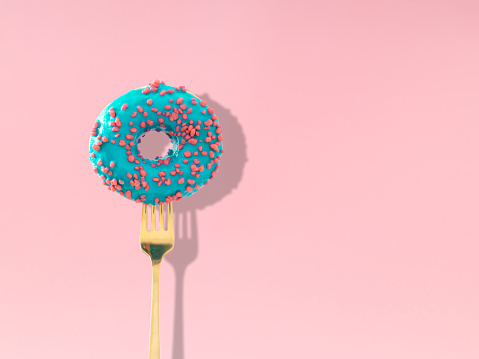 Yummy blue glazed donut pricked on a fork on pastel pink background. Creative art. Contemporary style. Minimal concept of food with copy space. Donut aesthetic background.