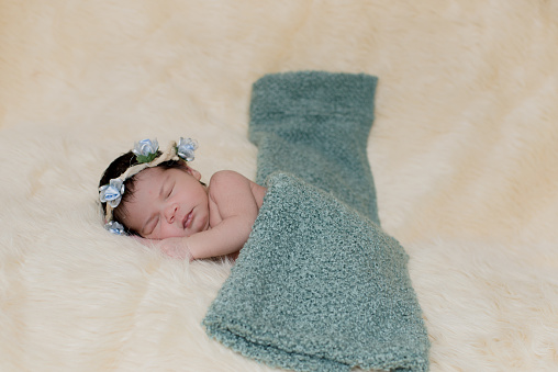 Newborn girl sleeps on the bed with a wreath on her head and covered with a green blanket