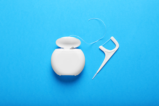 Container with dental floss and pick on light blue background, flat lay. Mouth hygiene