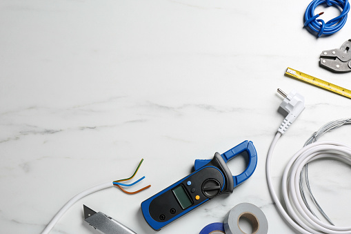 New wires and electrician's tools on white marble table, flat lay. Space for text