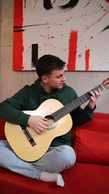 A young high school student plays the guitar in his spare time at his home