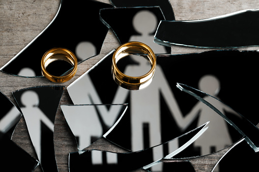 Divorce concept. Human figures reflected in broken mirror and wedding rings on wooden table