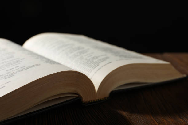 istock Open Bible on wooden table against black background, closeup 1786576789
